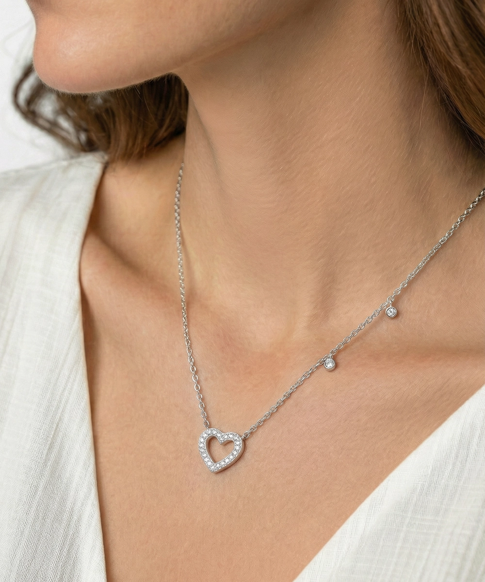 Silver heart-shaped necklace worn by a person with a white top