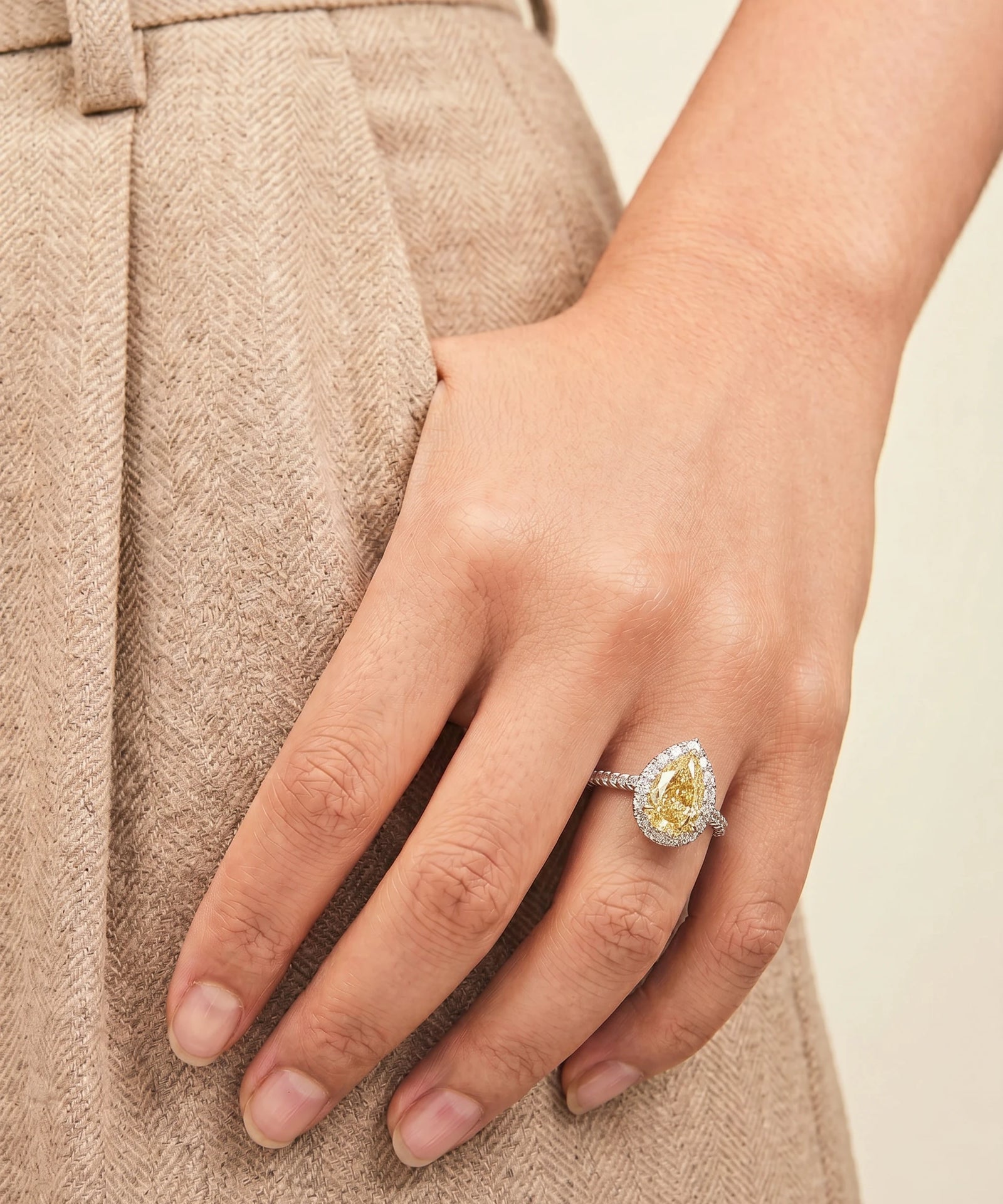 Close-up of a hand wearing a ring with a yellow gemstone against a neutral background