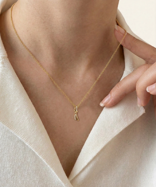Gold necklace with a unique pendant worn by a person against a neutral background