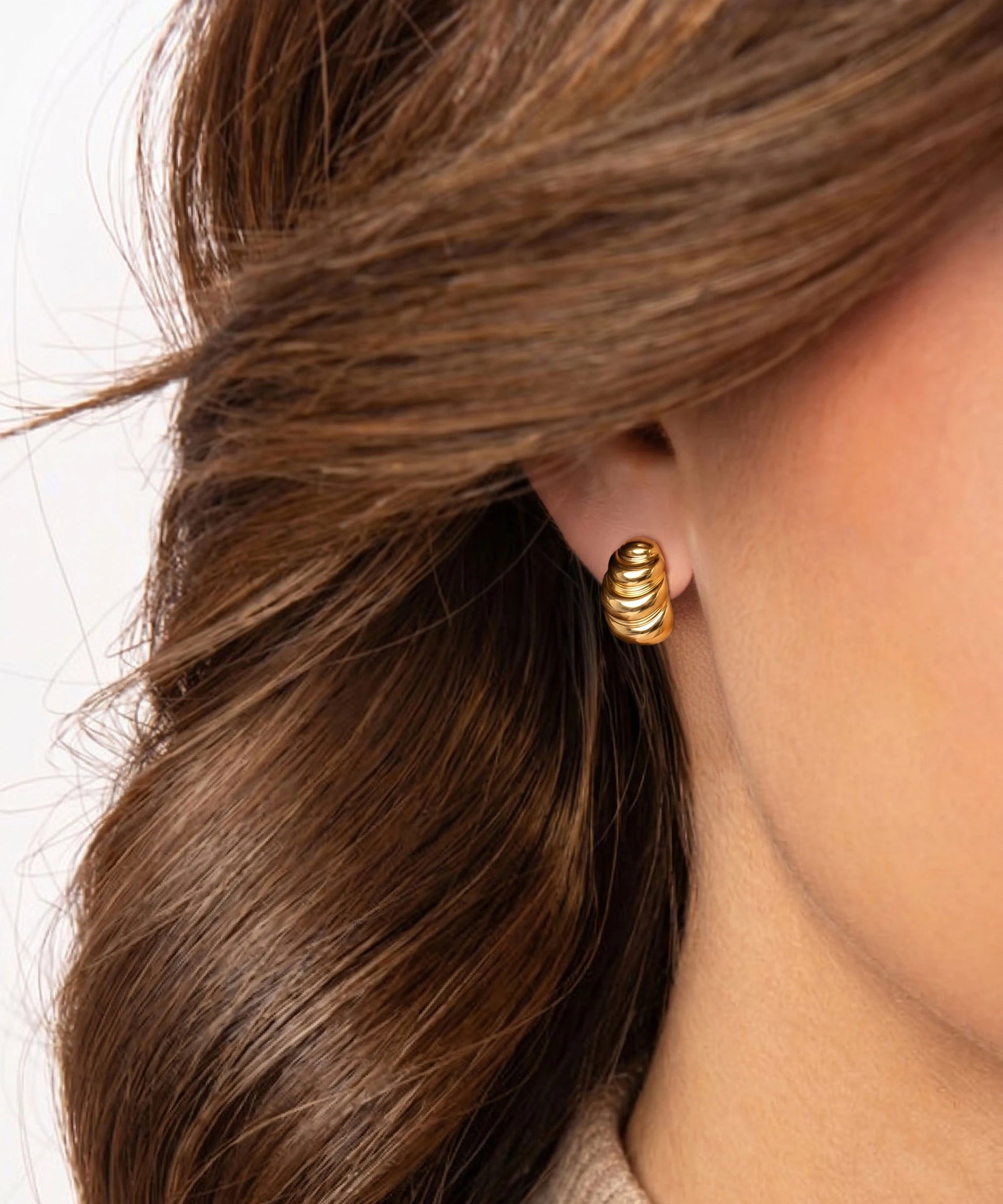 Gold spiral earring worn by a person with brown hair on a white background