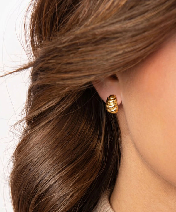 Gold spiral earring worn by a person with brown hair on a white background