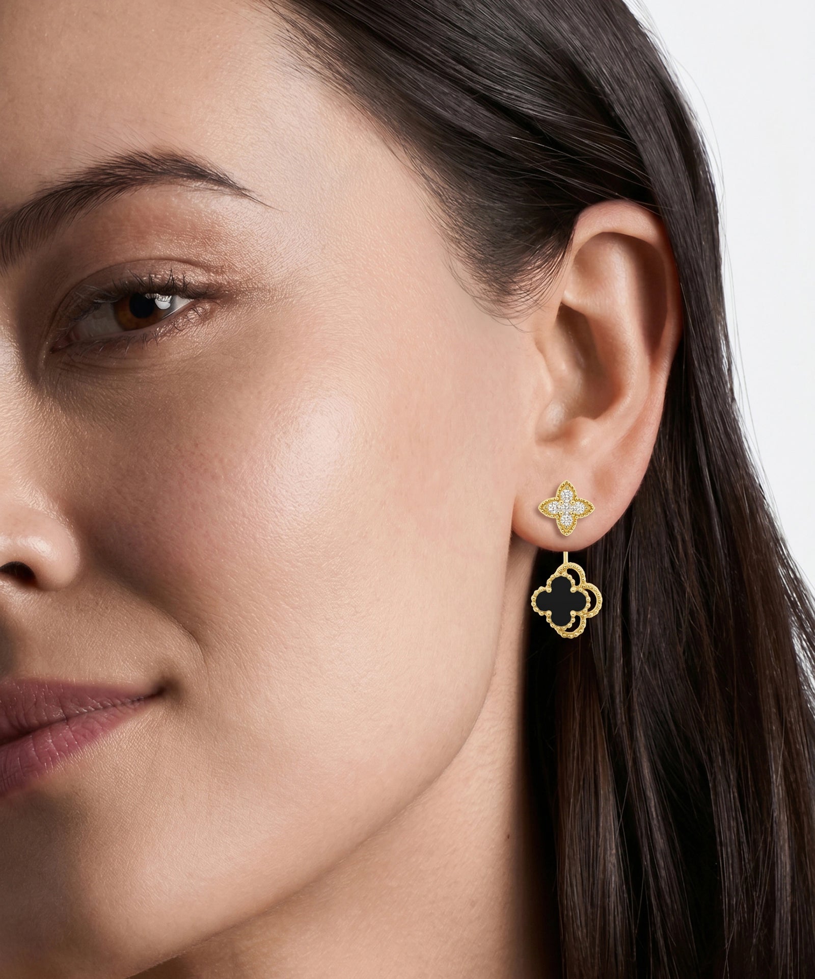 A close-up of a woman's ear wearing a gold four-leaf clover stud earring with a dangling openwork four-leaf clover charm.
