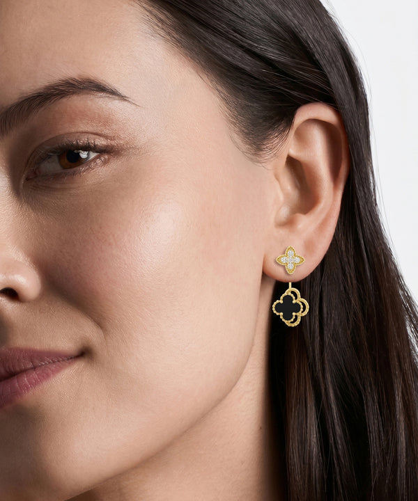 A close-up of a woman's ear wearing a gold four-leaf clover stud earring with a dangling openwork four-leaf clover charm.
