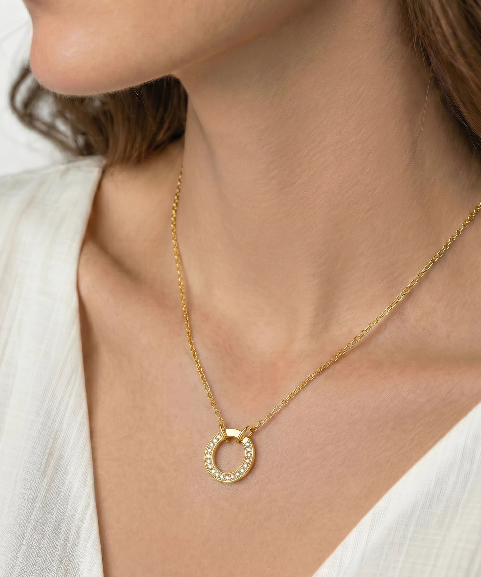 Gold necklace with a circular pendant worn by a person against a neutral background