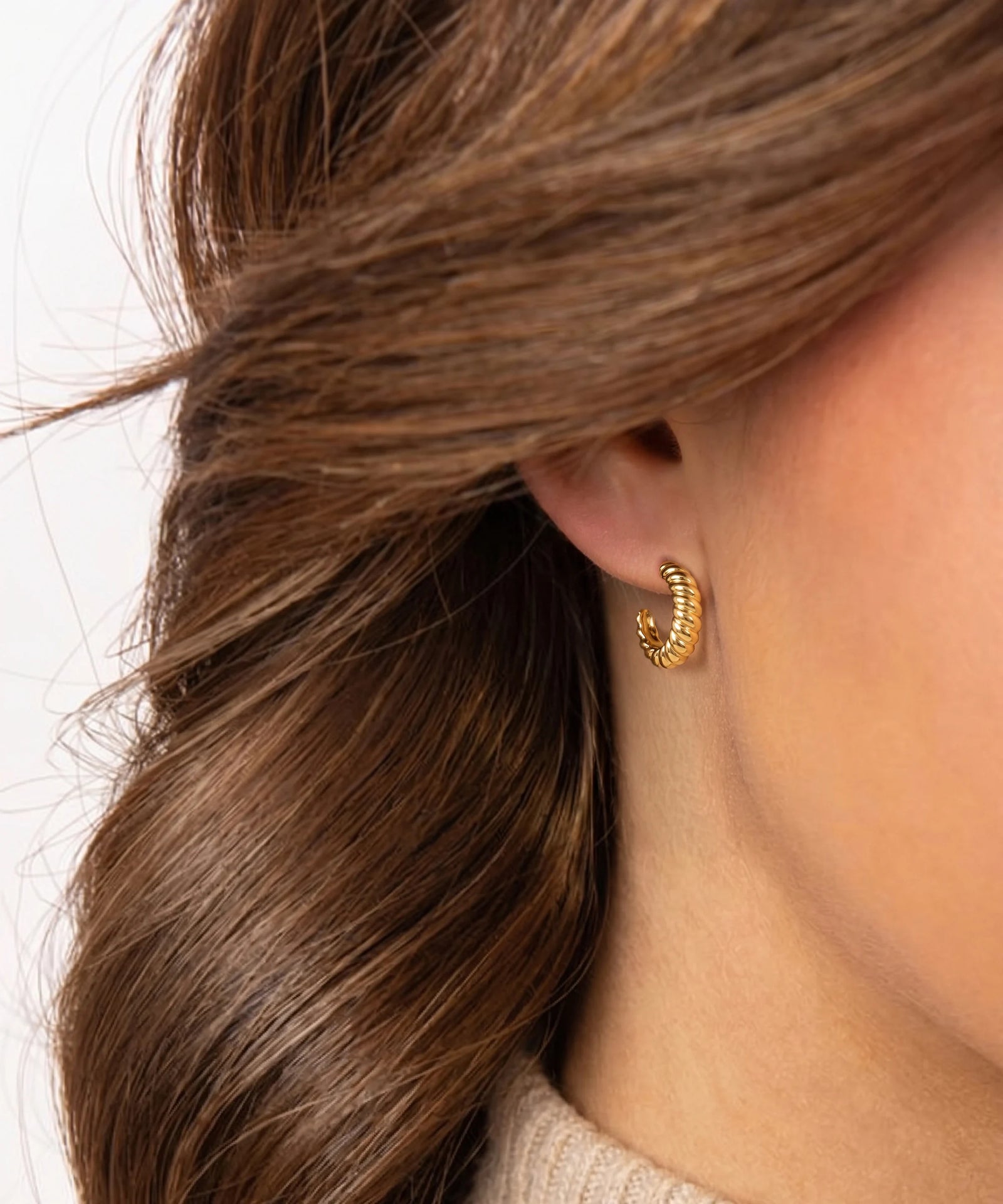 Close-up of a person wearing a gold hoop earring with hair partially covering the ear.