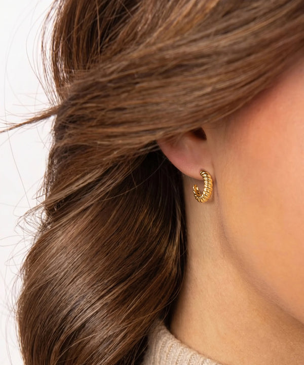 Close-up of a person wearing a gold hoop earring with hair partially covering the ear.