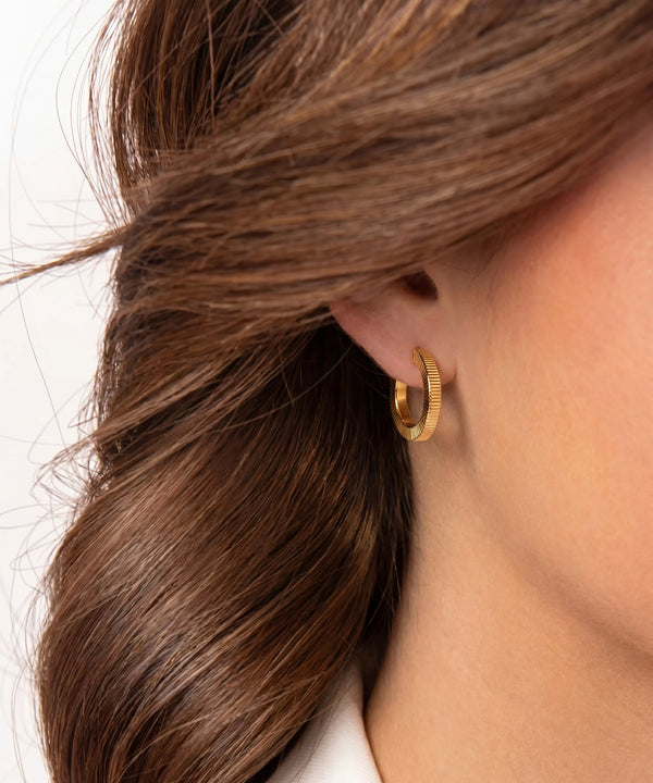 Close-up of a person wearing a gold hoop earring with hair partially covering the ear.