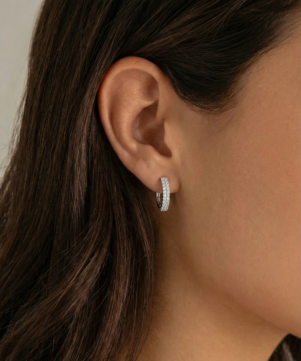 Close-up of an ear wearing a silver hoop earring with dark hair and neutral background
