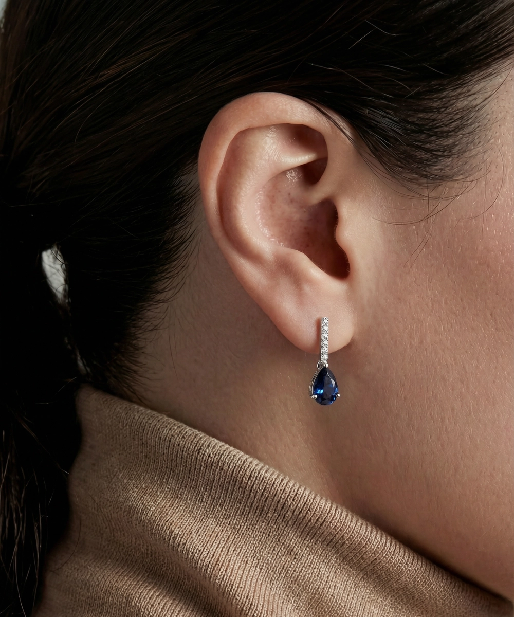 Close-up of an ear wearing a blue teardrop earring with a blurred background
