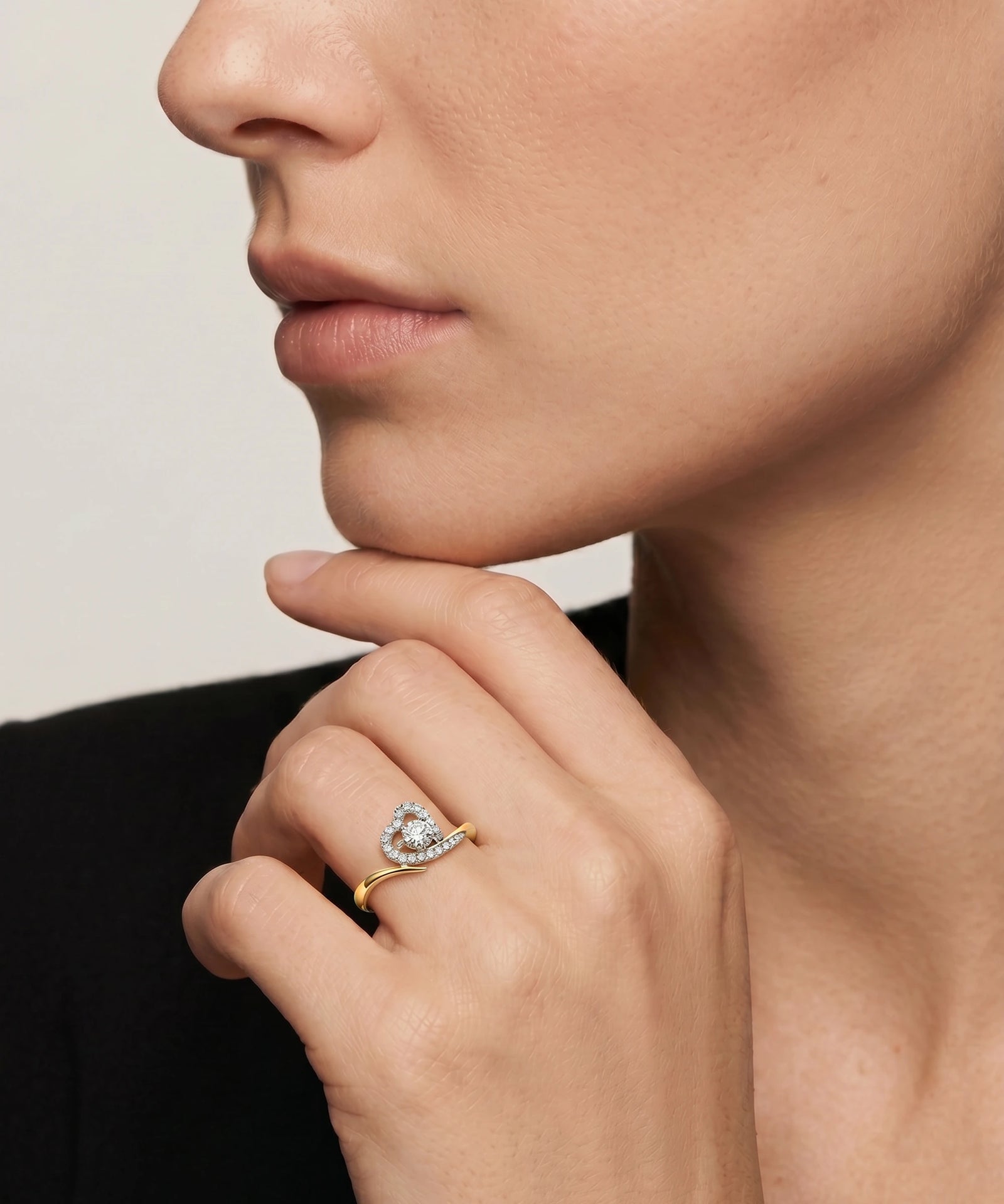 Close-up of a hand wearing a gold ring with a diamond, touching the chin against a neutral background.