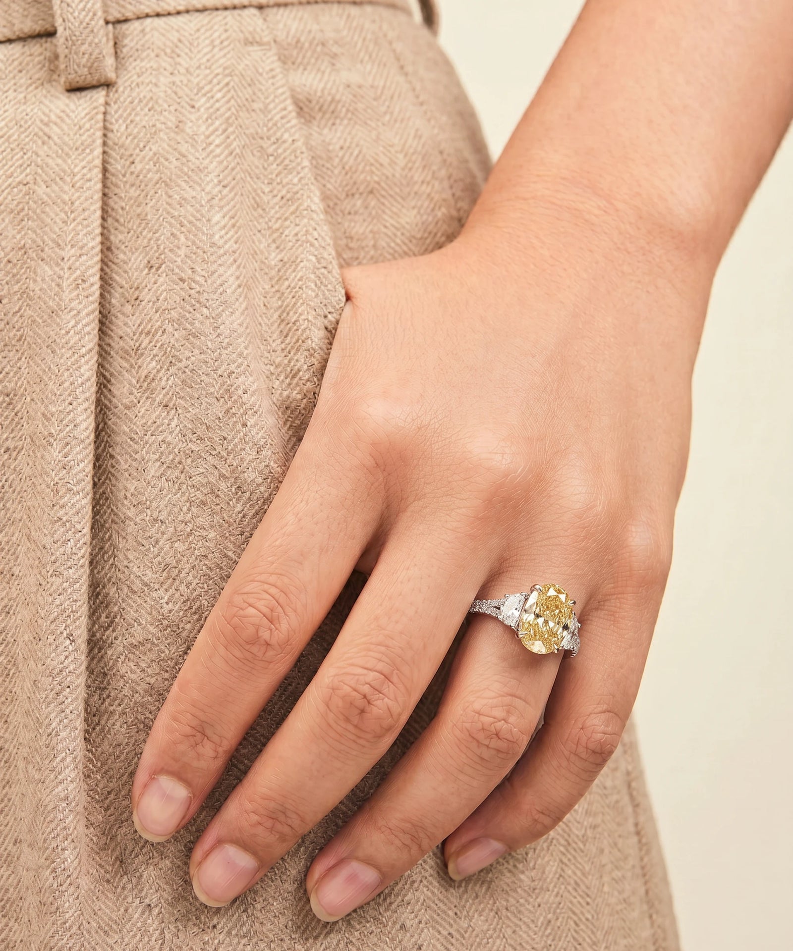 Close-up of a hand wearing a ring with a yellow gemstone against a neutral background