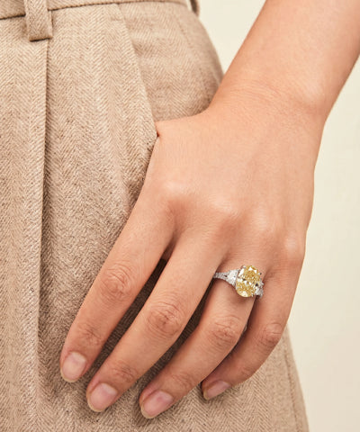Close-up of a hand wearing a ring with a yellow gemstone against a neutral background - alternate view