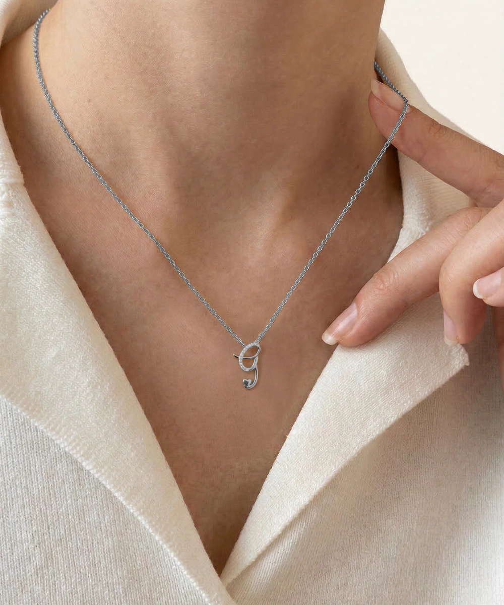 Silver necklace with a letter 'S' pendant worn by a person against a neutral background