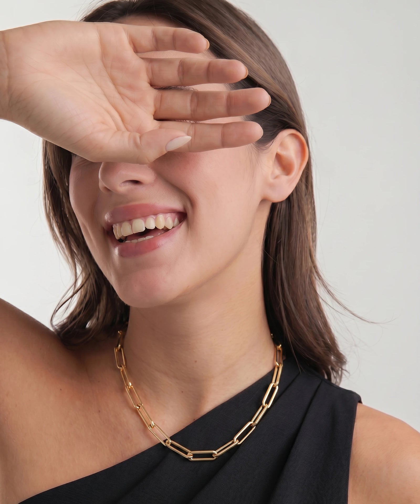 Woman wearing a gold chain necklace with a plain background