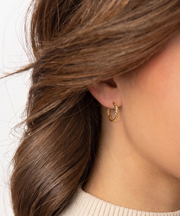 Close-up of a person wearing a gold hoop earring with hair partially covering the face.
