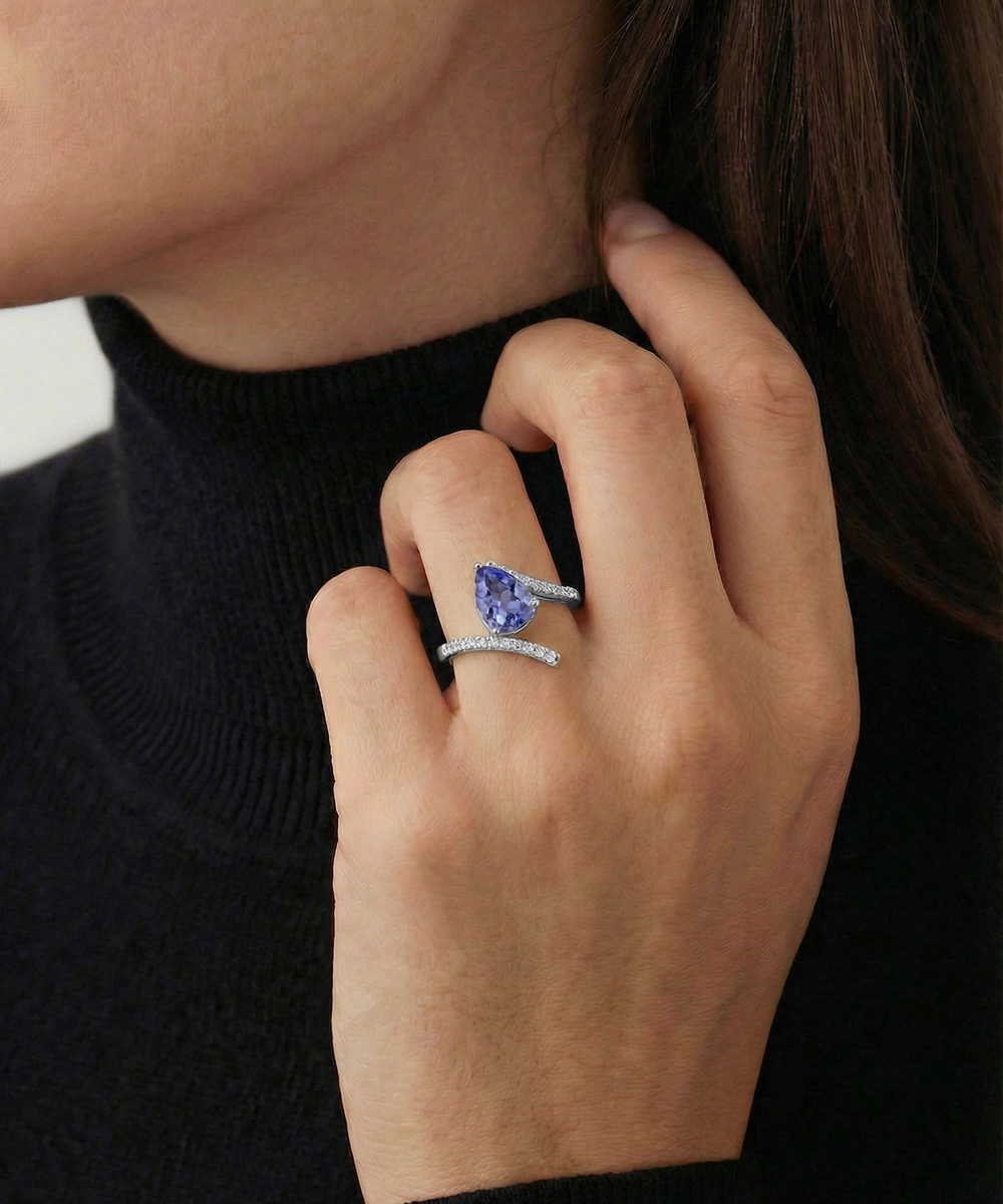 Close-up of a hand wearing two rings with a blue gemstone on a dark background