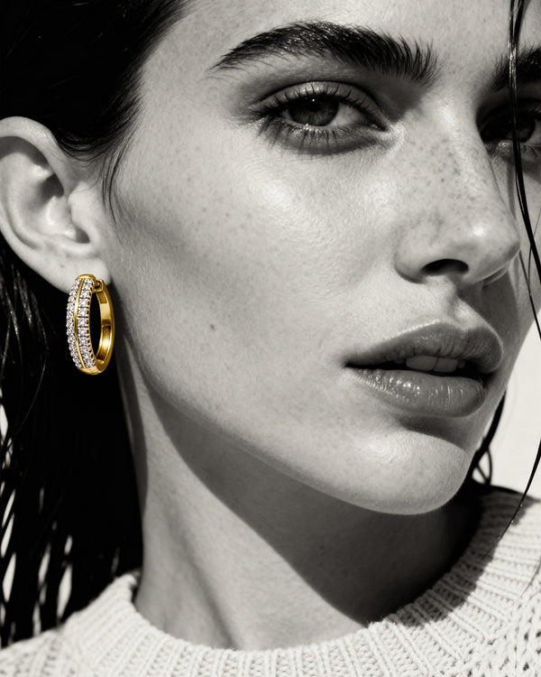 Close-up of a woman wearing gold hoop earrings with a black and white background