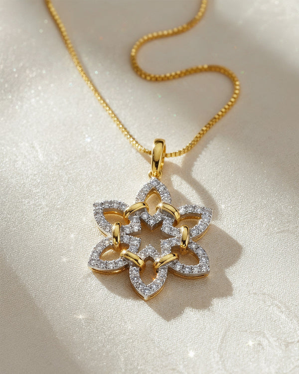 A gold necklace with a floral-shaped pendant, featuring intertwined gold and diamond-encrusted petals, is displayed on a soft, light-colored surface.