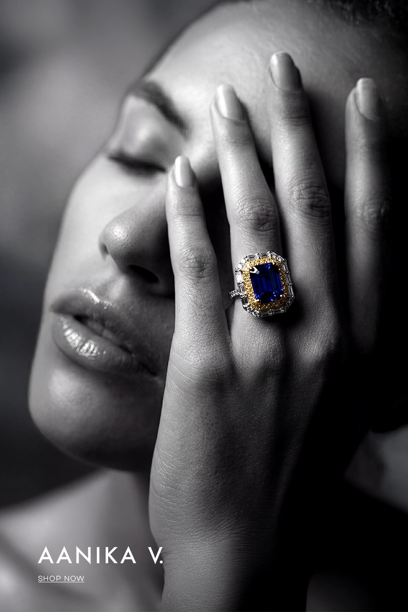 Close-up of a woman's face with a hand covering her eye, wearing a ring with a blue gemstone, with 'Aanika V.' branding.