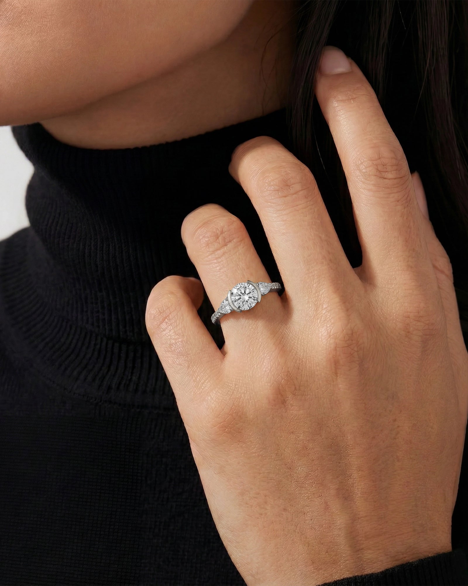 Close-up of a hand wearing a diamond ring against a neutral background