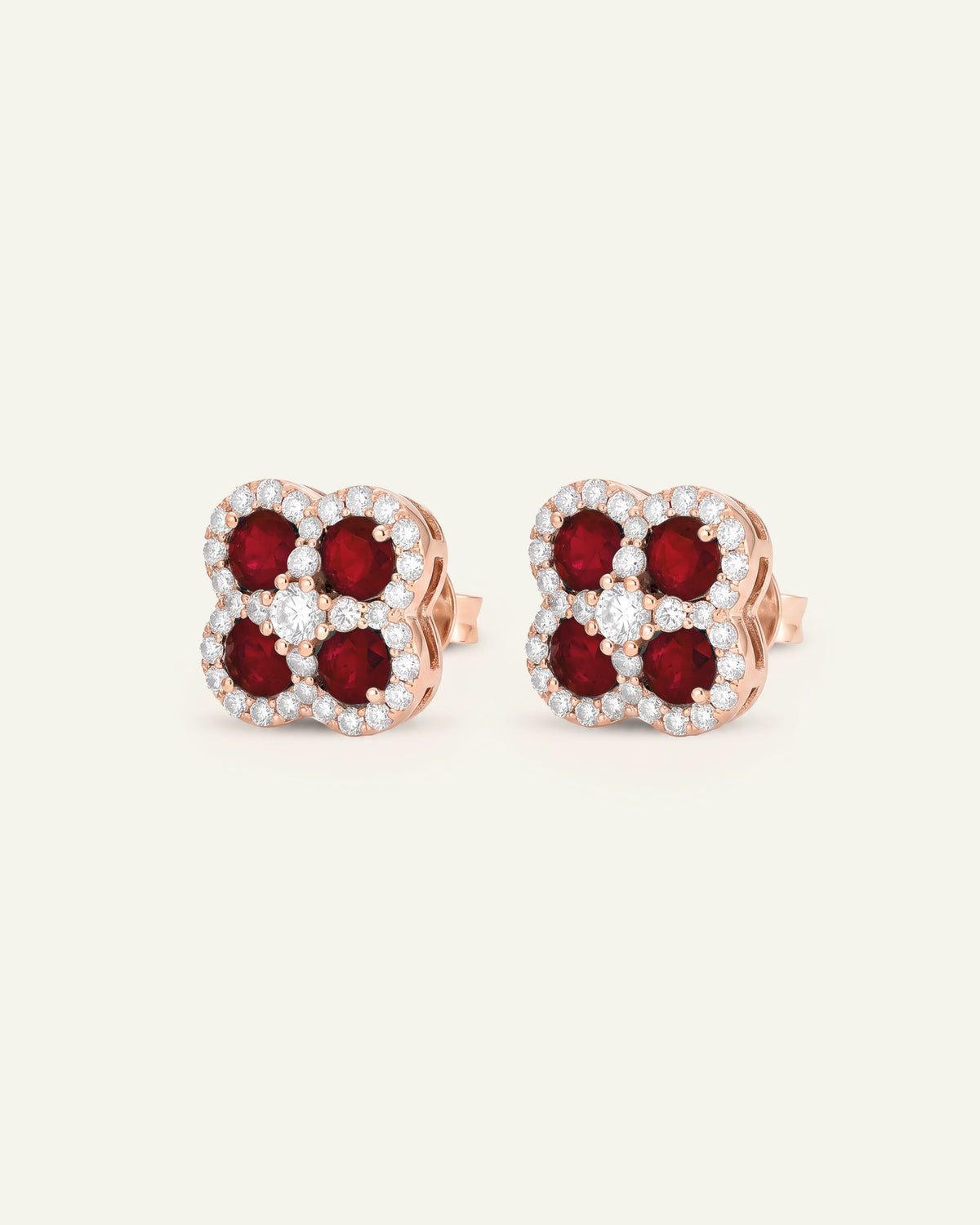 A pair of rose gold stud earrings featuring four round-cut deep red gemstones surrounded by small clear stones, set against a plain off-white background.