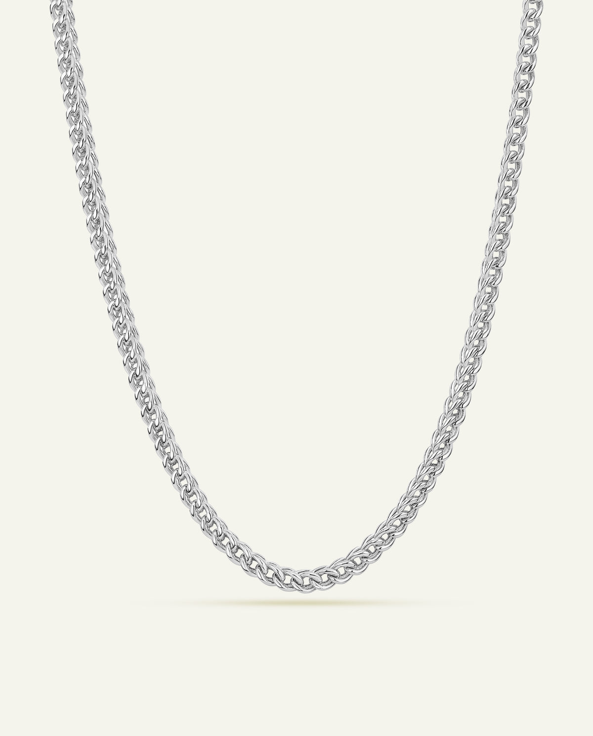 A silver-toned metal chain necklace with a curb link pattern, displayed in a U-shape against a solid, warm off-white background.