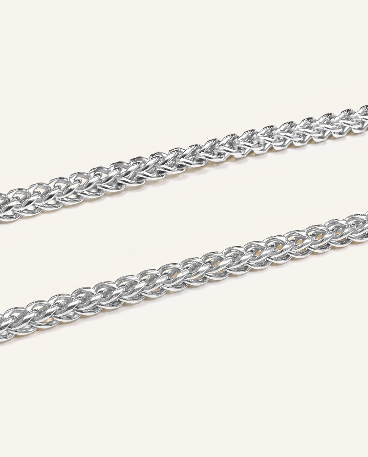 A close-up of a silver-toned metal chain with interlocking oval links, shown diagonally on a plain off-white background.