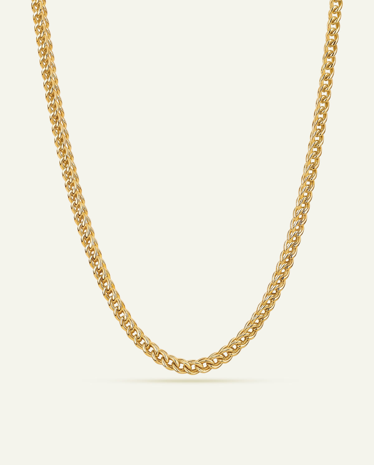A gold-toned curb chain necklace displayed in a clean, centered studio shot against a light cream background.