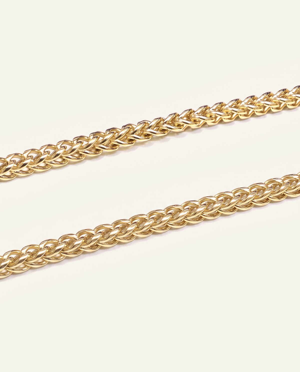 A close-up of a gold-toned curb chain shown in two parallel strands against a clean, off-white background.