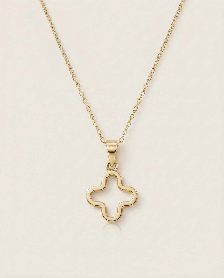 A delicate yellow gold chain necklace featuring an open four-leaf clover pendant on an off-white background.