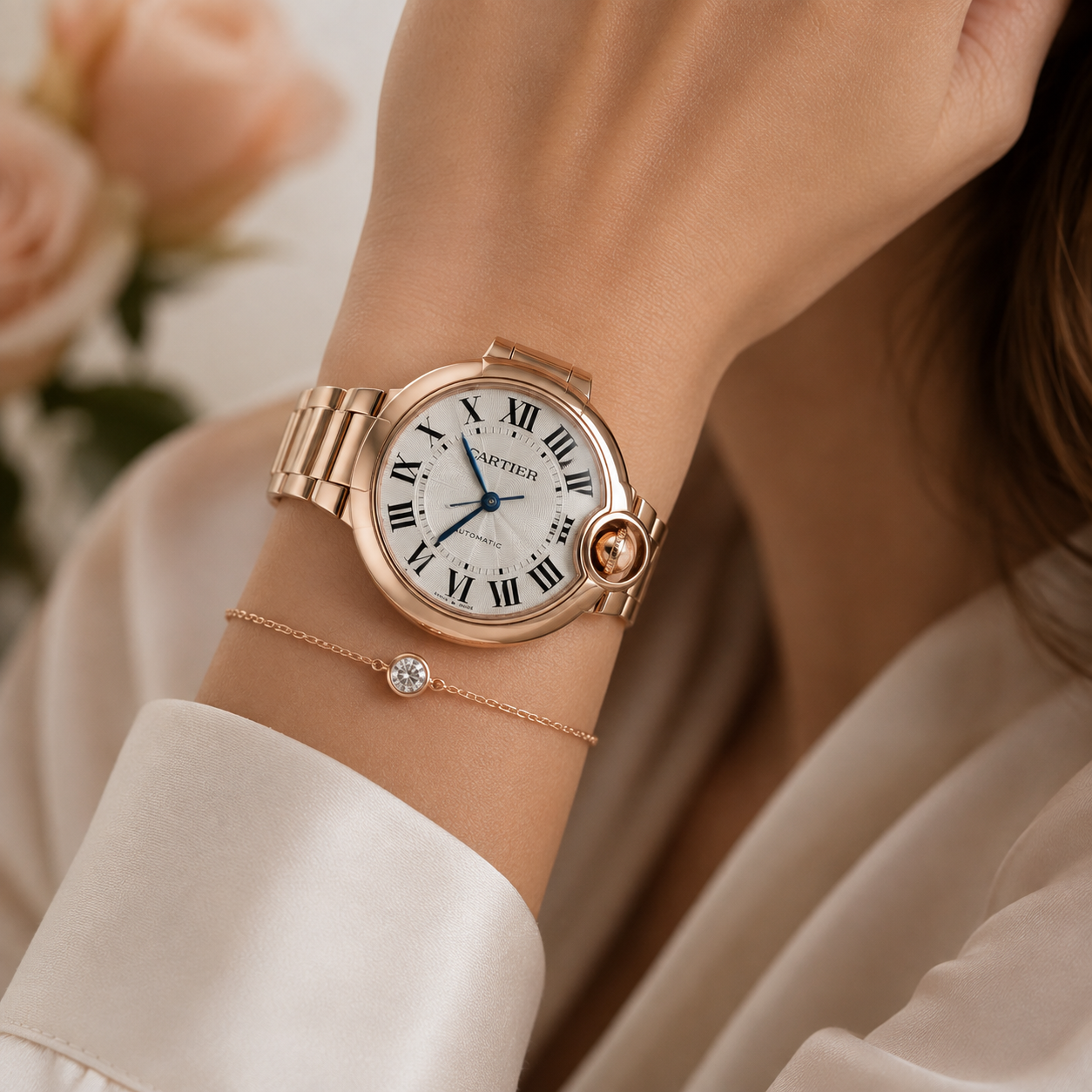 A close-up lifestyle shot of a Cartier Ballon bracelet watch on a woman's wrist, styled with a delicate Cartier bracelet. The watch features a rose gold-toned metal bracelet, a white dial with black Roman numerals, and a signature round bezel with a rose gold cabochon.