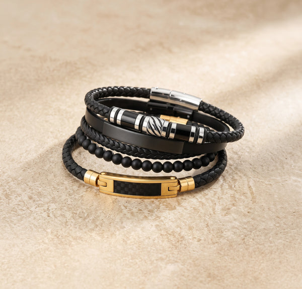 Stack of black leather and beaded bracelets with gold and silver accents on a beige surface