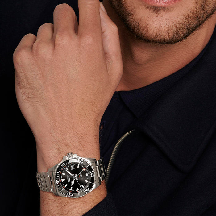 Man wearing a silver watch with a black face on a dark background