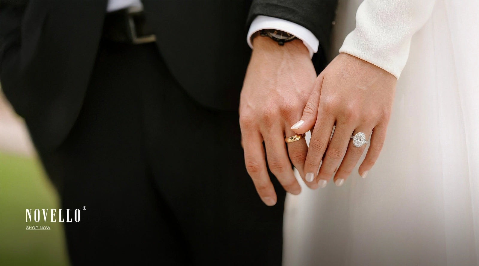 Close-up of hands with wedding rings, one gold and one silver, against a blurred background. Brand 'Novello' visible.