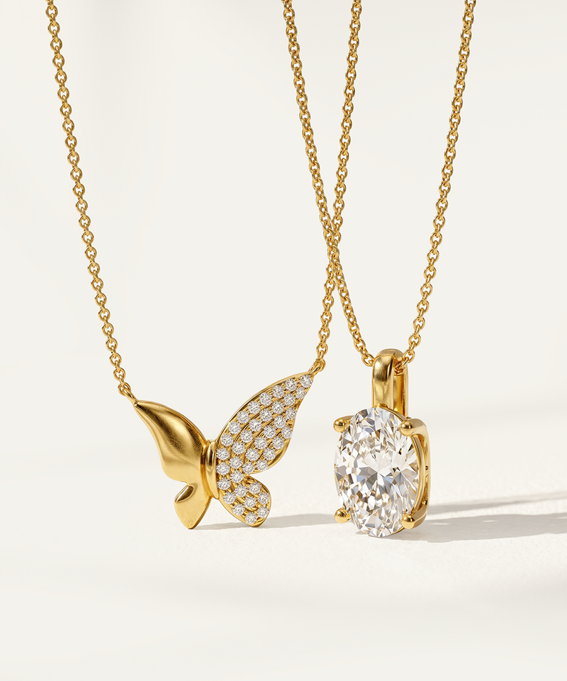Gold butterfly pendant and diamond pendant on gold chains against a white background