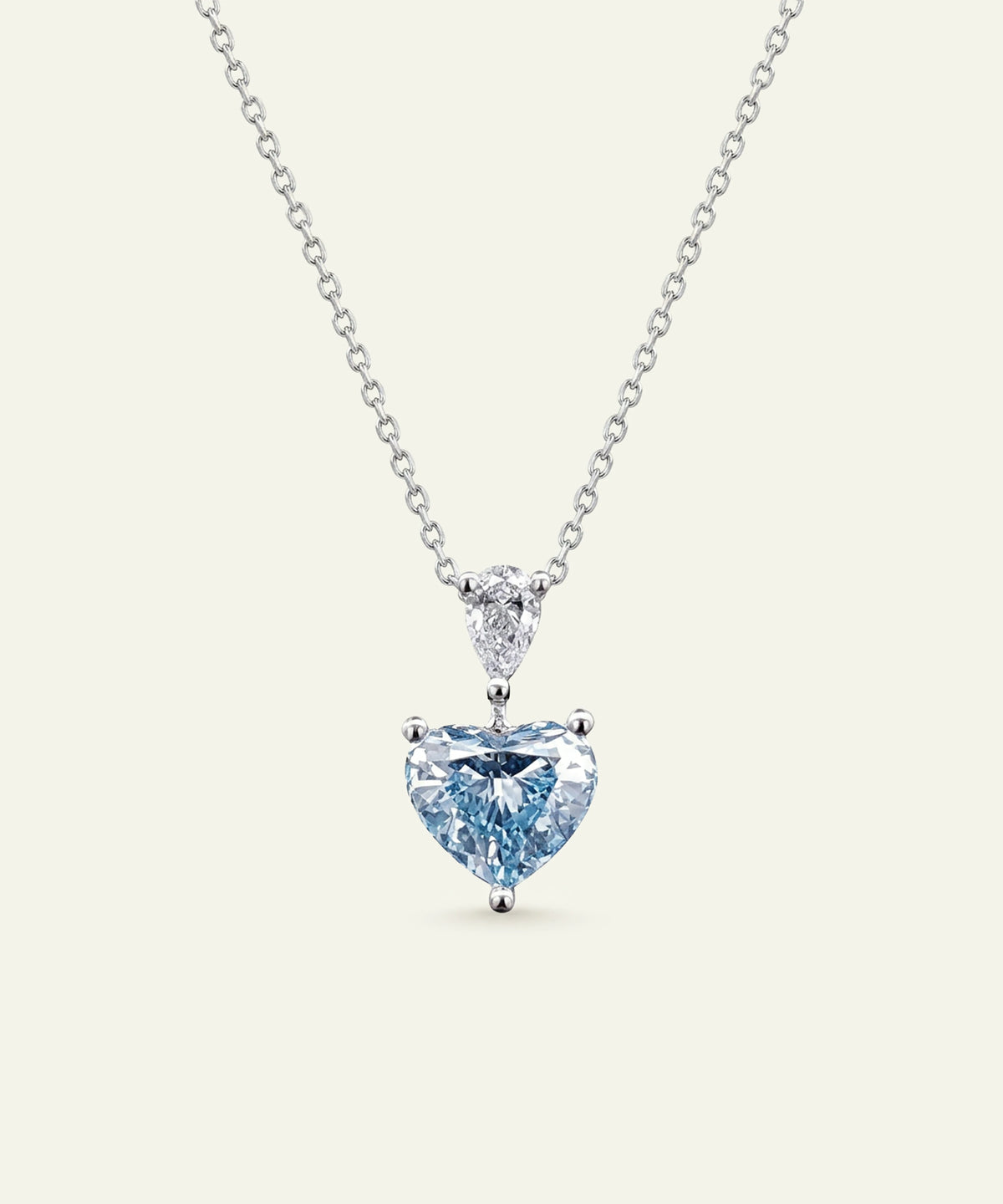 A heart-shaped light blue gemstone pendant necklace in a silver setting on a delicate silver chain, presented against a solid off-white background.