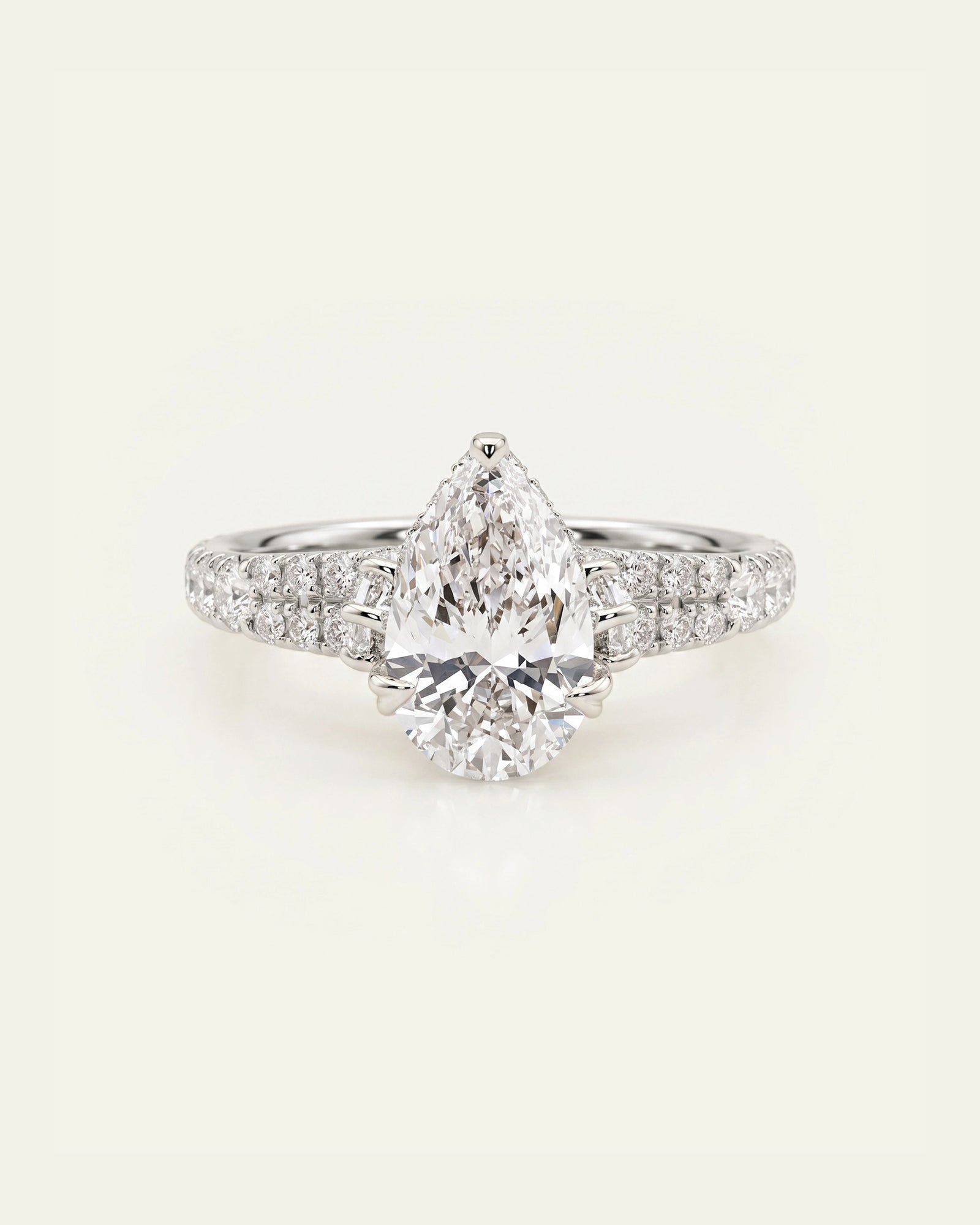 A pear-cut diamond engagement ring with a pavé band set with small round diamonds, shown on a light cream background.