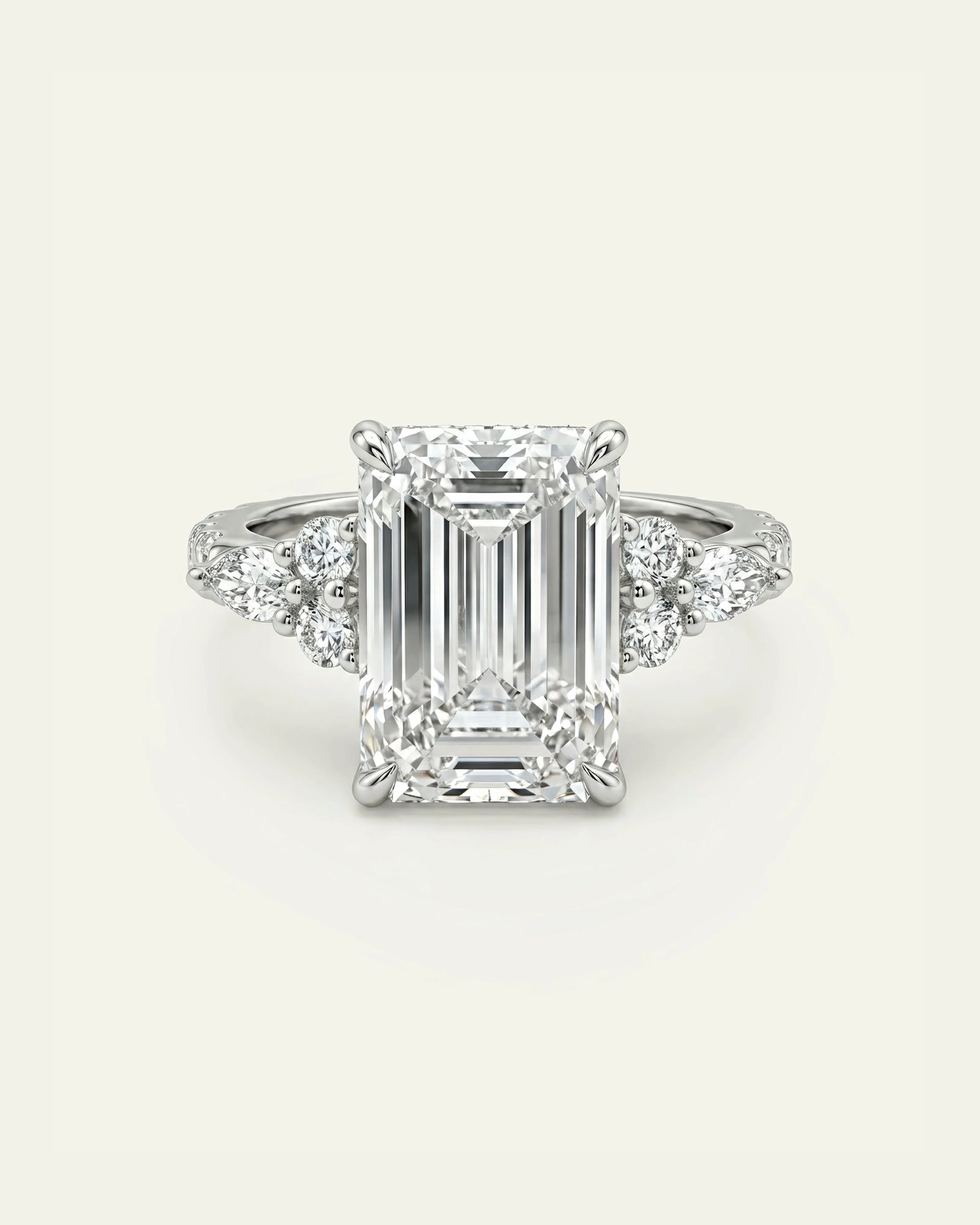 An emerald-cut diamond engagement ring with a silver-toned band featuring small side diamonds, centered on a light cream background.