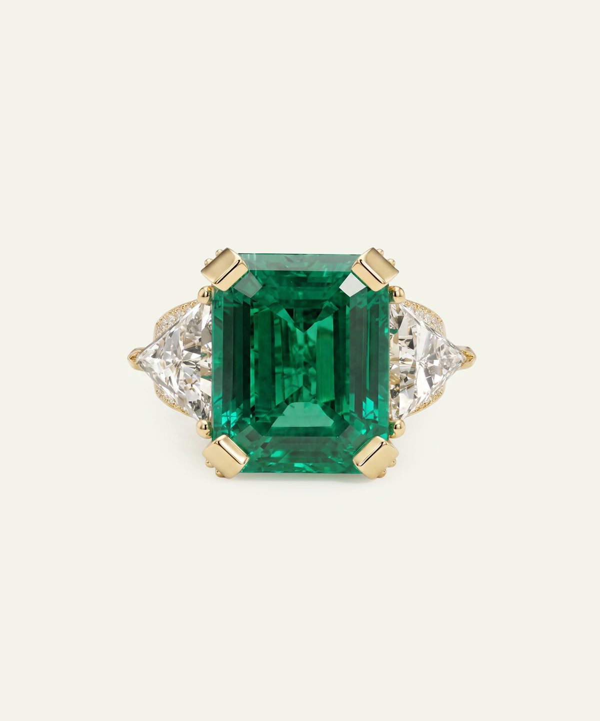 An emerald-cut green emerald ring with a yellow gold setting and diamond accents on either side, set against a solid off-white background.