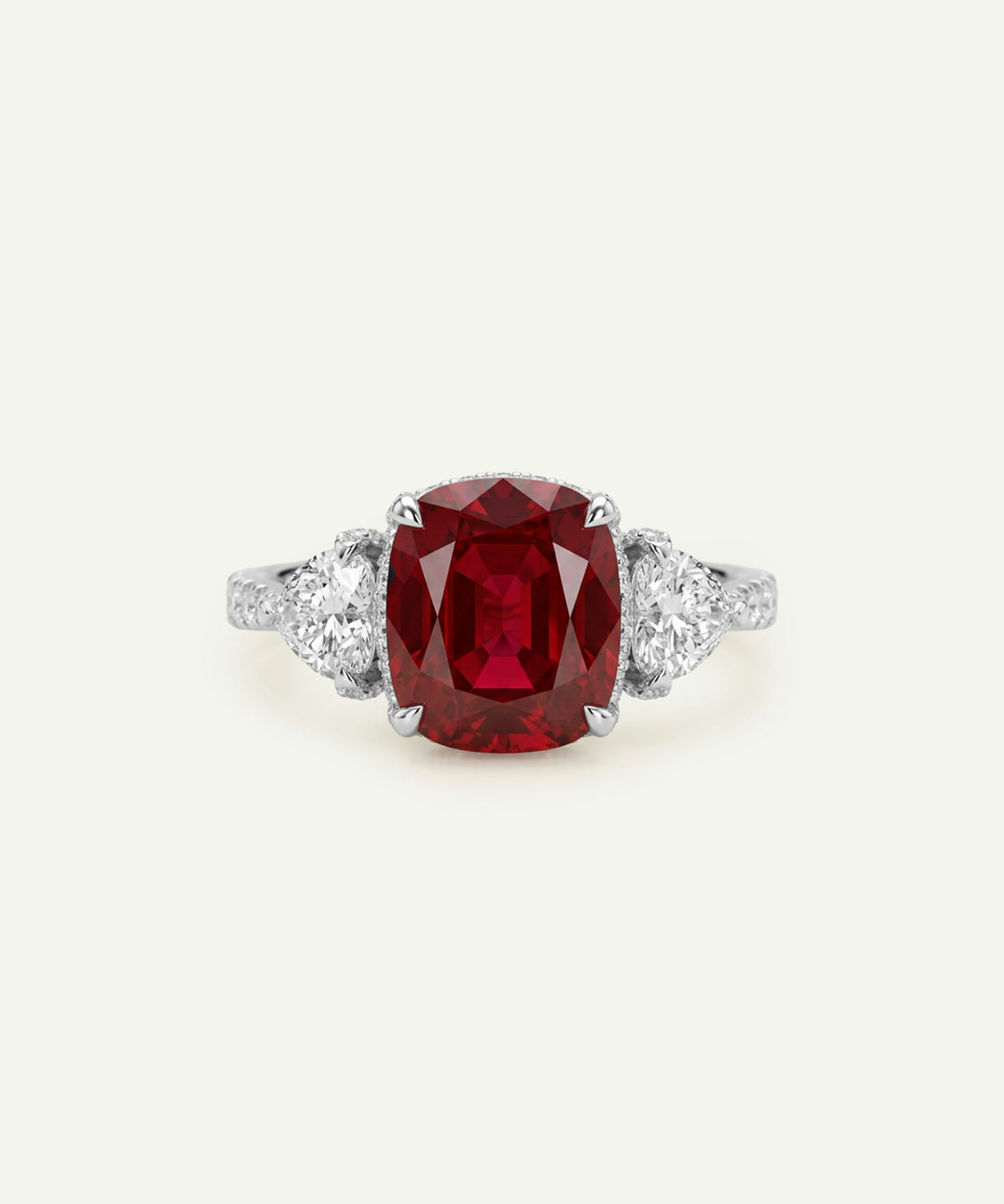 A silver three-stone ring featuring a large cushion-cut red ruby center stone and two small round-cut diamonds on either side of the band, set against a light cream background.