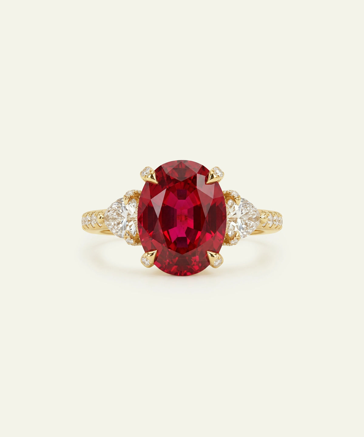 An oval-cut red ruby ring set in yellow gold with diamond accents on the shoulders, photographed on a light cream background.