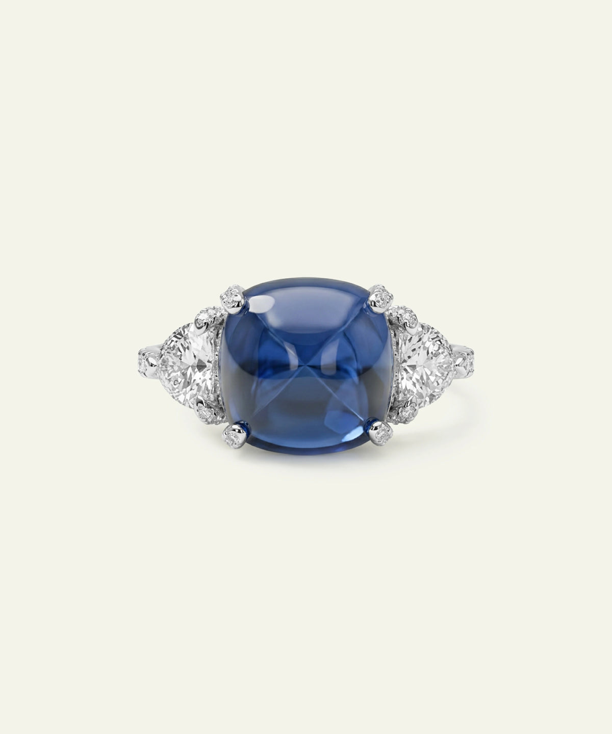 A cushion-cut blue sapphire ring with a silver-toned setting accented by small round diamonds on either side, shown against a solid off-white background.