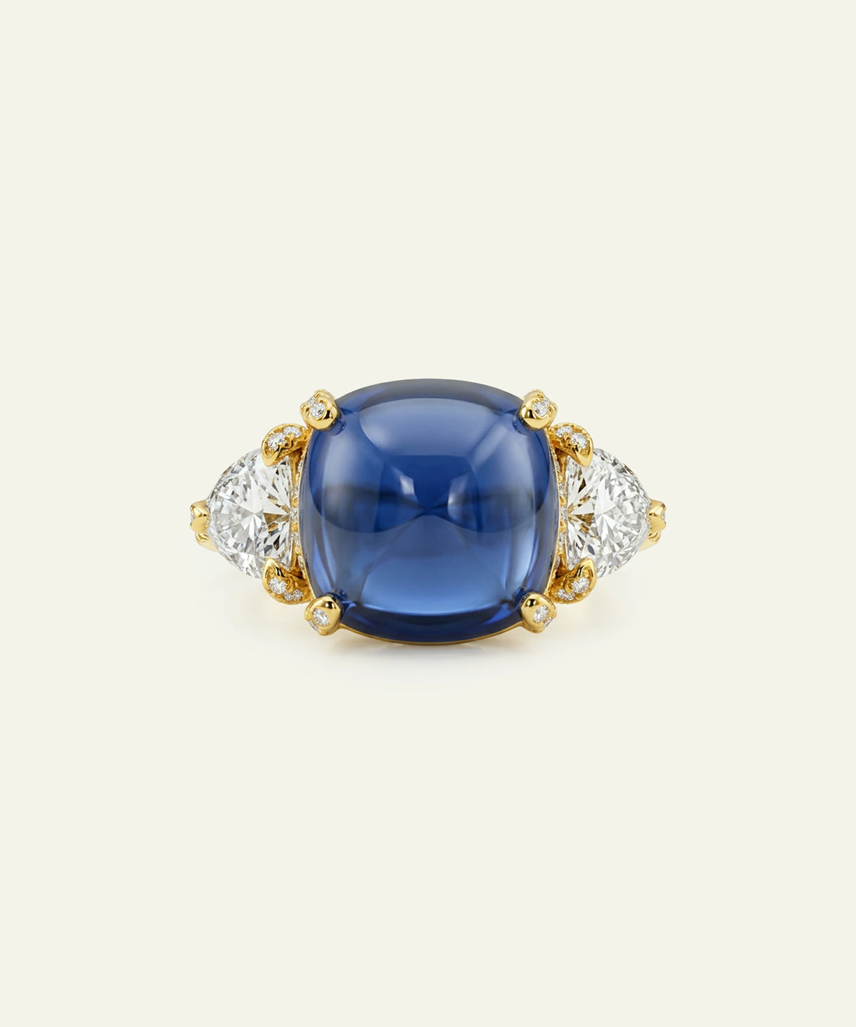 A luxury ring featuring a large cushion-cut deep blue cabochon gemstone in a yellow gold setting, flanked by two marquise-cut clear diamonds on a cream background.