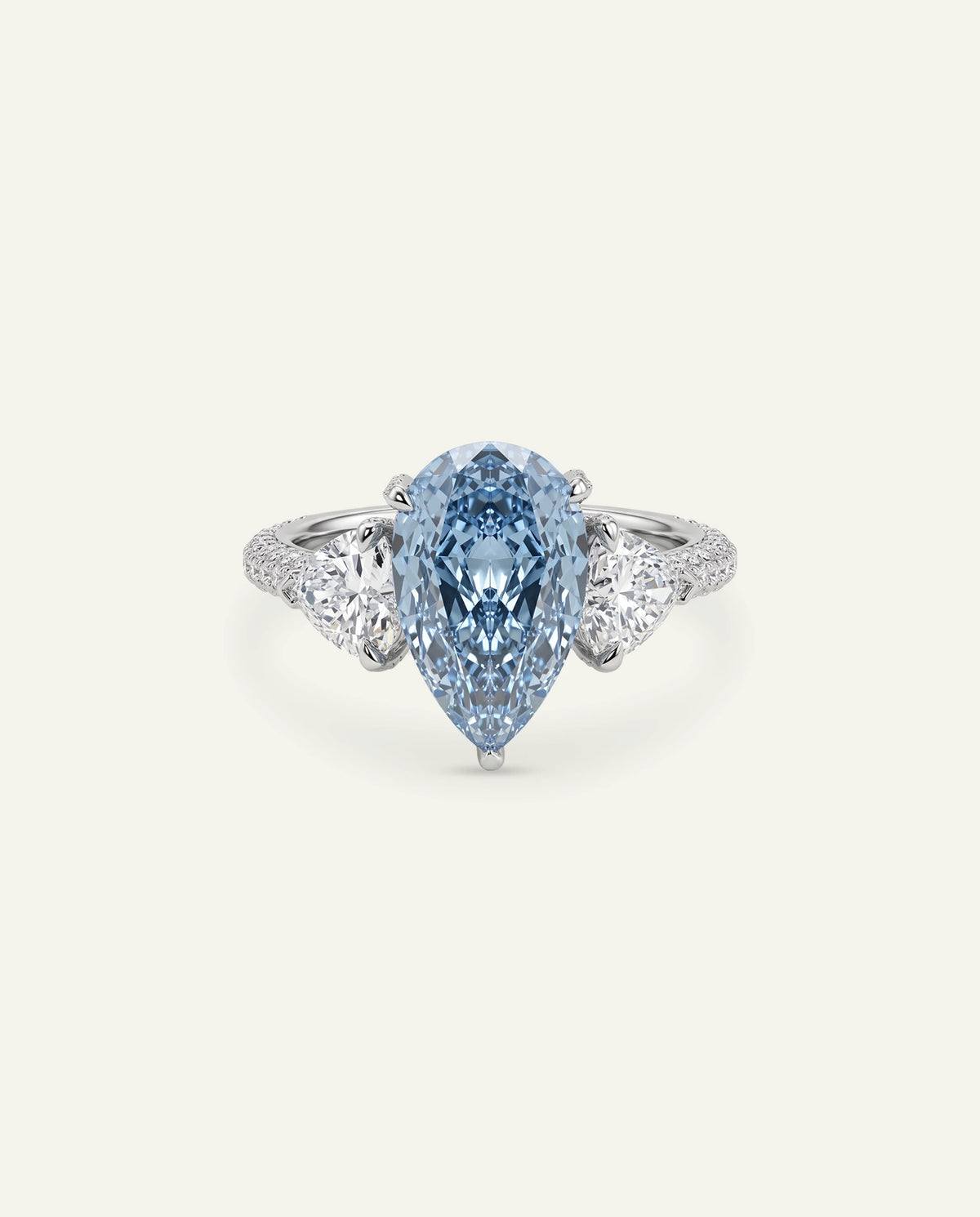 A pear-cut light blue gemstone ring set in a silver-toned band with small clear stones along the shoulders, centered on a plain off-white background.