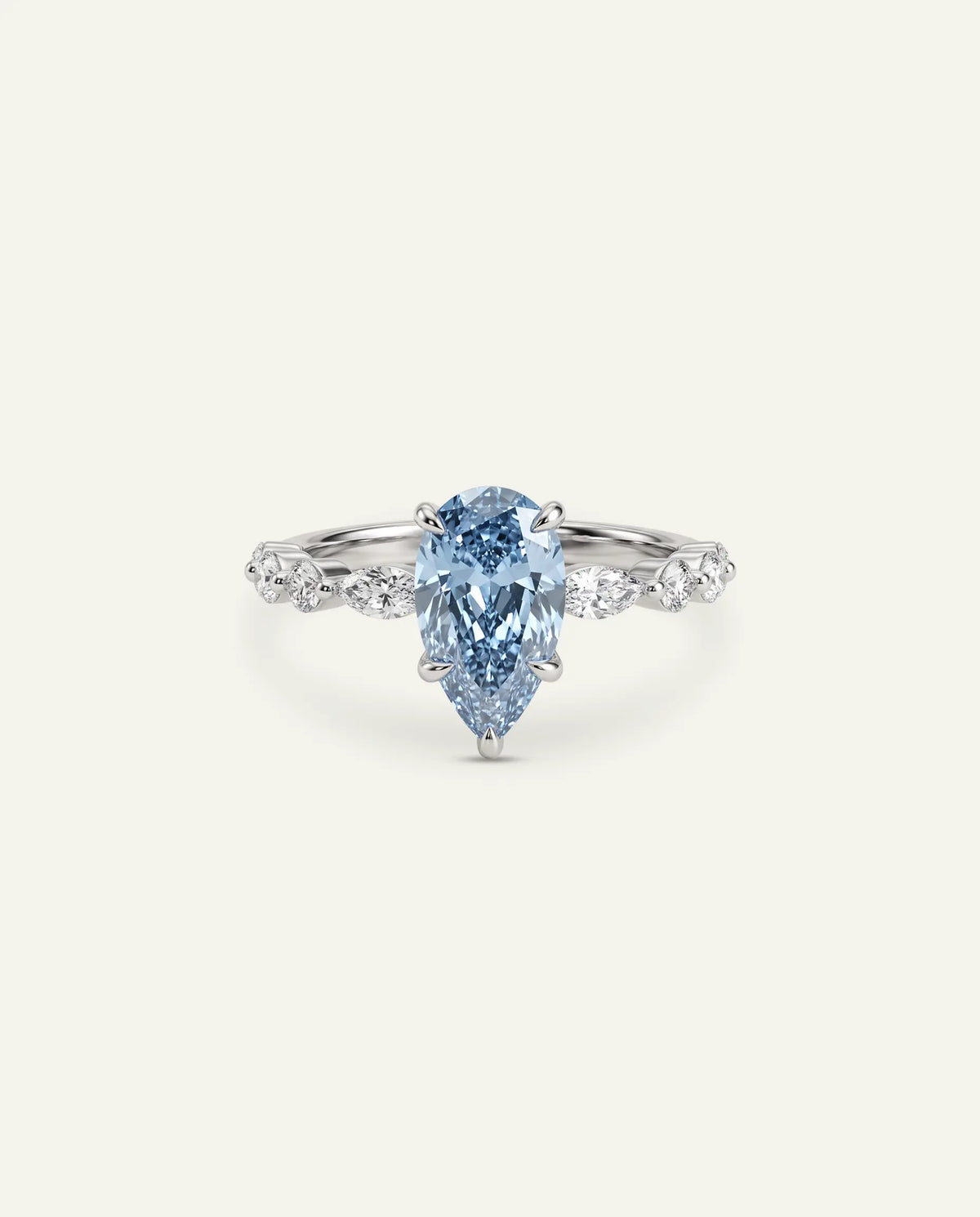 A pear-cut light blue gemstone ring set in a silver-toned band with small clear stones along the shoulders, centered on a plain off-white background.