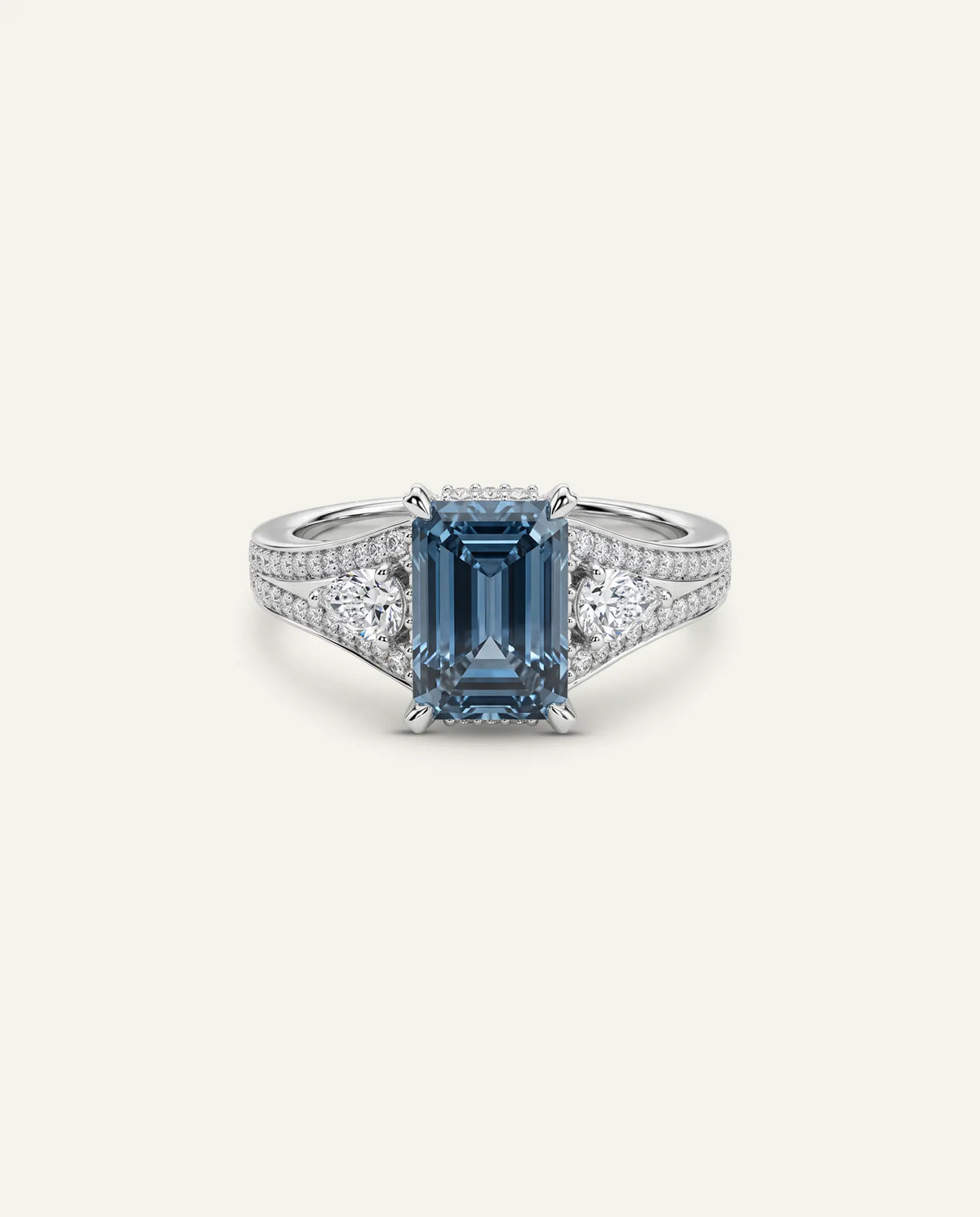 An emerald-cut blue sapphire ring set in a silver-toned band with pavé diamonds, centered on a light cream background.