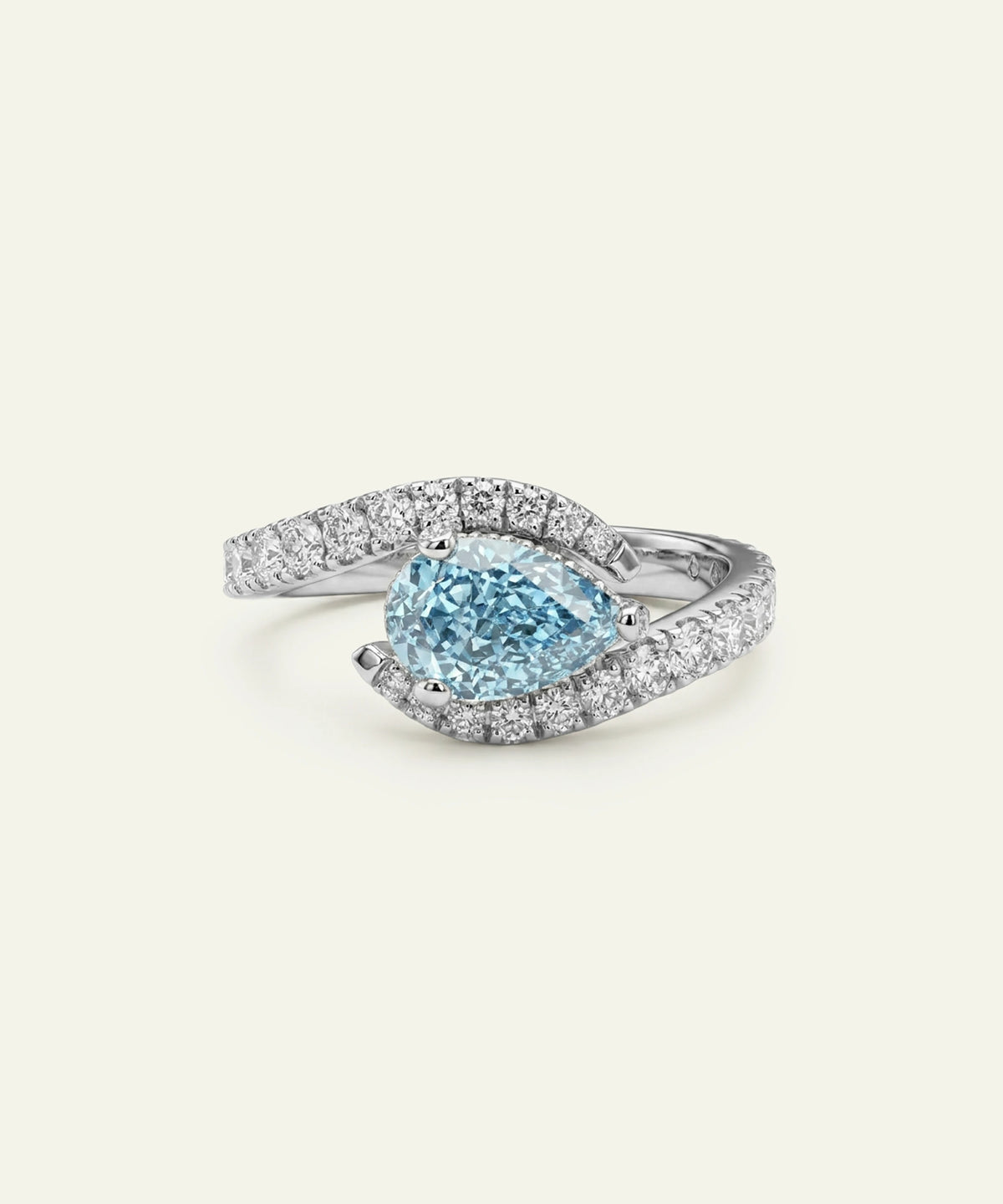 A pear-cut light blue gemstone ring with a silver-toned pavé band, photographed on a clean, solid off-white background.