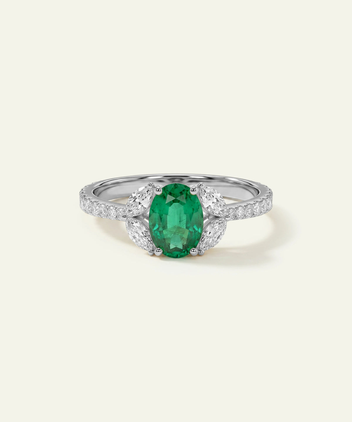 An oval-cut emerald green gemstone ring set in a silver-colored metal with pavé diamond accents on the shoulders, presented on a light cream background.