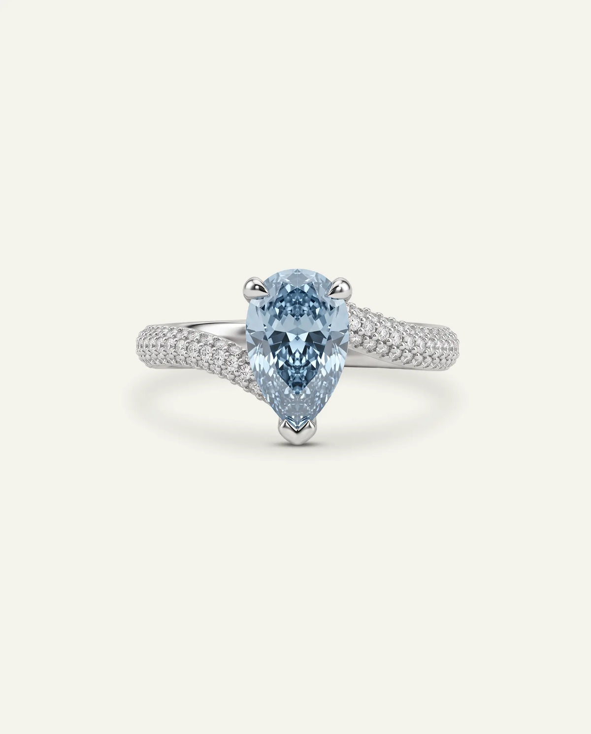 A silver ring featuring a pear-cut light blue diamond center stone with a multi-row pavé diamond band, set against a light cream background.