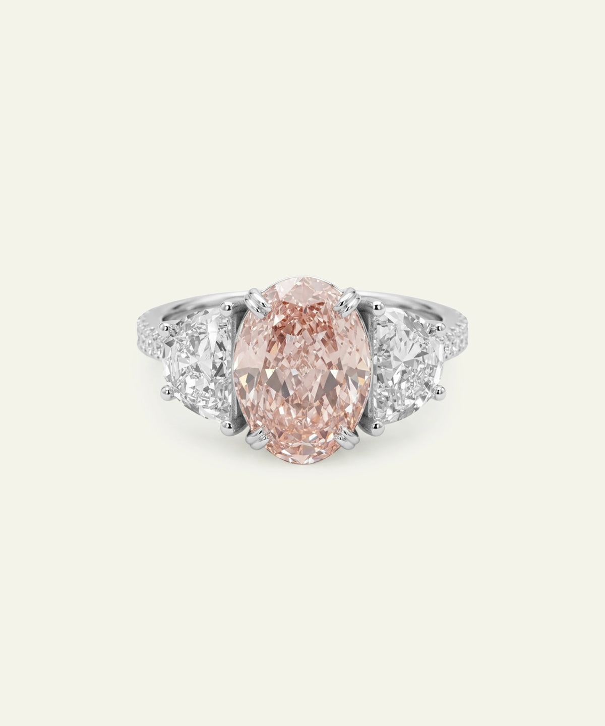 A silver ring featuring an oval-cut pink diamond center stone flanked by two half-moon side diamonds and a pavé diamond band.